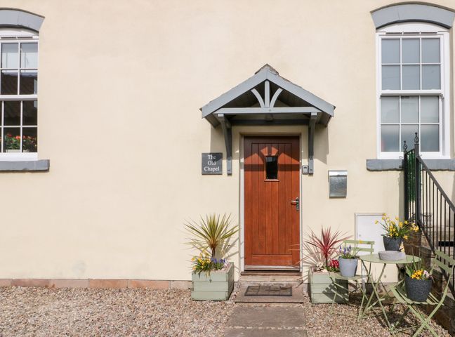 A front door with two windows and plants in pots with a table and chairs outside at Old Chapel in Cloughton