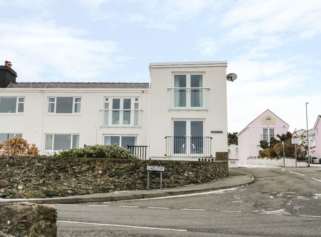 A white two storey house with balconies and a stone wall next to a road at Harbour View in Cemaes Bay