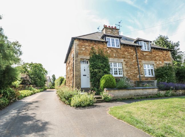 A stone house with white windows and a white door surrounded by greenery and flowers at Wren Cottage in Wing near Uppingham Rutland