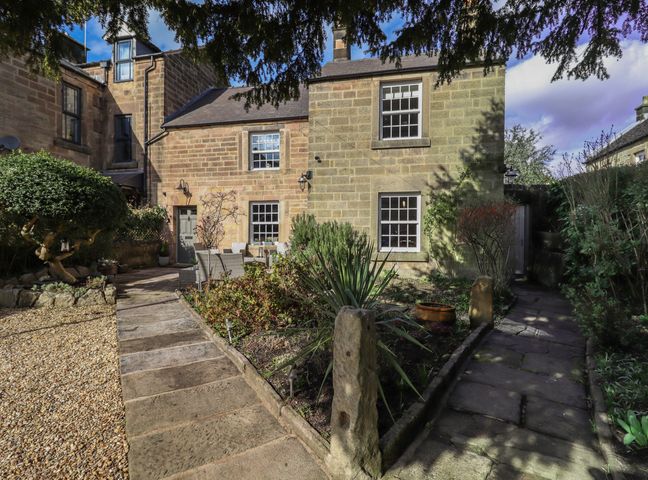 A stone house with a garden and paved paths leading to outdoor seating at Rose Cottage in Matlock