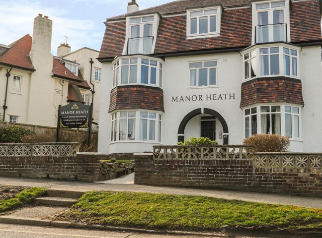 The exterior of a white building with brown tiled roof and bay windows with a sign for Manor Heath luxury holiday apartments in Scarborough