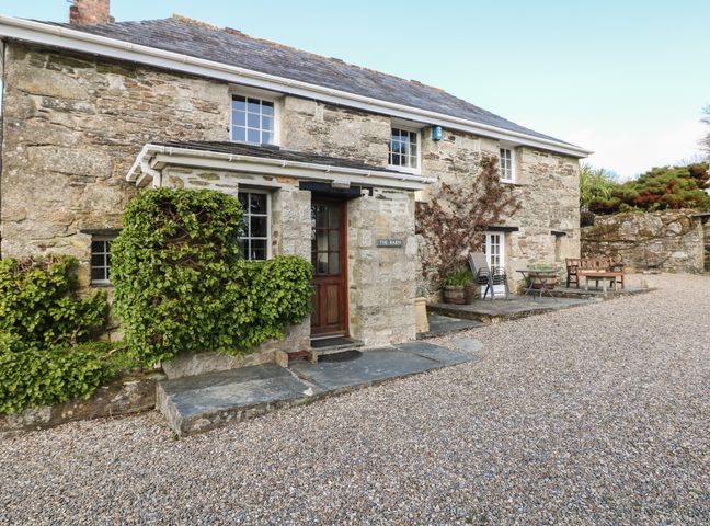 Exterior of a stone building with wooden door green climbing plants and gravel ground at Trevenning Barn Near Port Isaac