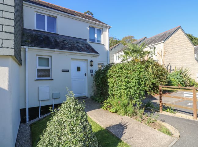 The exterior of a two-story house with a white door and windows surrounded by bushes and greenery at Hedgehog Cottage in Falmouth