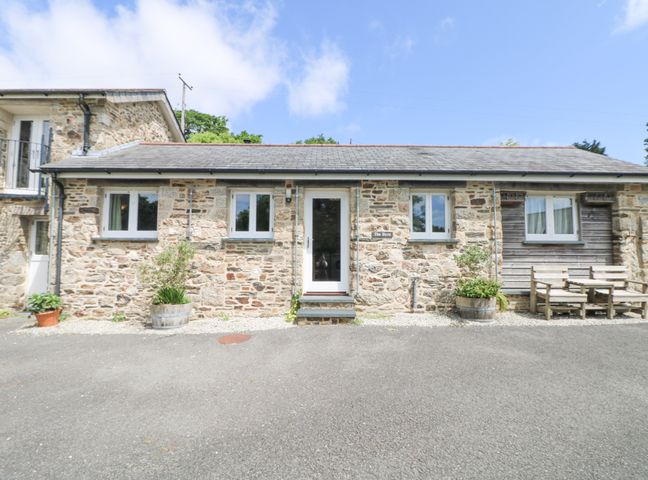 A stone cottage with three windows a door and outdoor wooden benches at The Byre in Lostwithiel