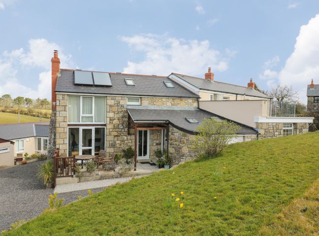 A stone house with a patio and outdoor furniture on a grassy slope at Mynheer Farm Barn Nr Portreath