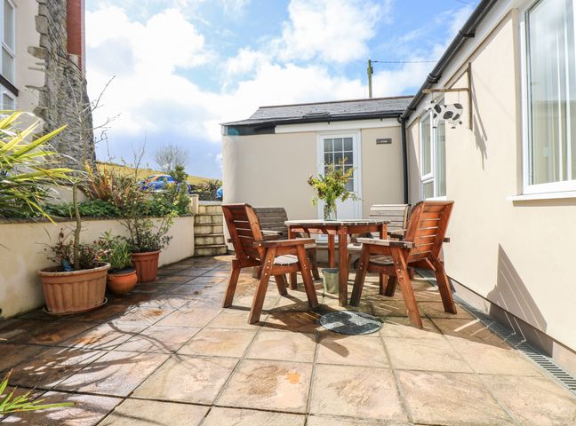 A patio with wooden chairs and a table with a plant in a vase and potted plants along the walls at Mynheer Farm Bowji Nr Portreath