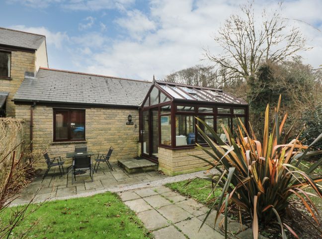 A stone house with a glass conservatory and outdoor seating area at Chy-Nans in Falmouth