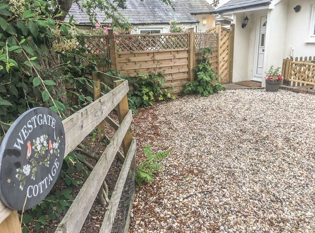 An outdoor area with a wooden fence gravel ground plants and a white door at Westgate Cottage in Sittingbourne