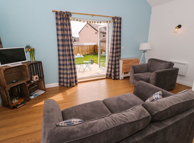 A living room with a grey sofa and armchair a wooden floor a small TV on wooden crates and a door leading to a garden at The Button Box in Golcar