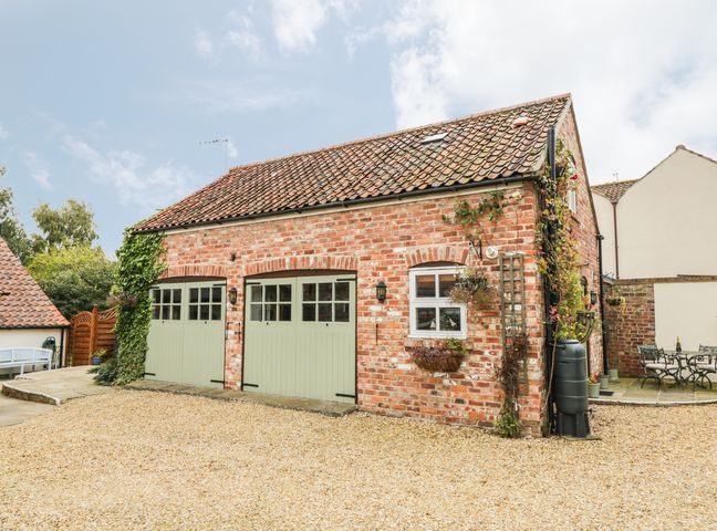 A brick garage with green doors and a gravel driveway at The Loft in Upper Dunsforth near Boroughbridge