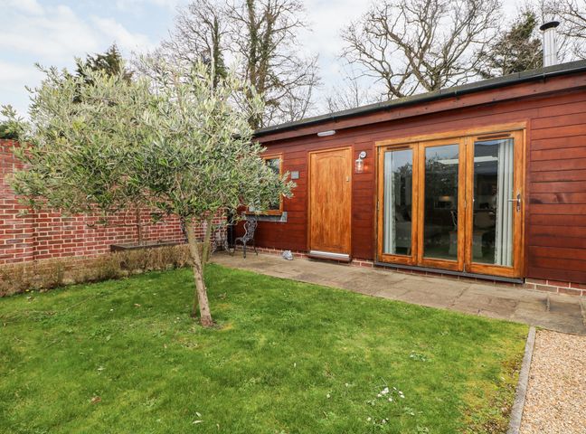A small garden with a tree and a wooden house with a door and large windows at Rabbit's Warren in Titchfield Common