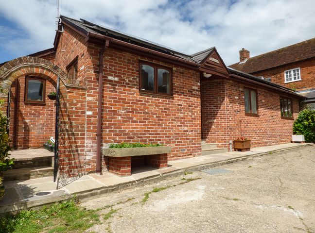 A brick building with windows and an arched gate leading to a patio with planters at 27 Swan Street in Boxford