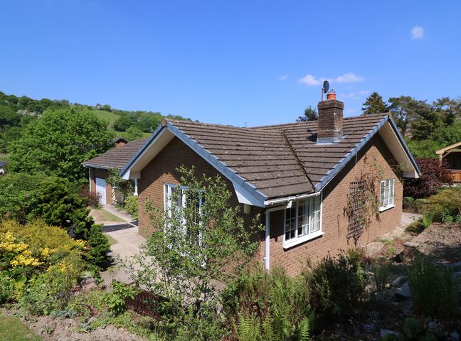 An exterior view of a single-story brick house with a tiled roof and surrounding garden at Pen Y Maes in Builth Wells