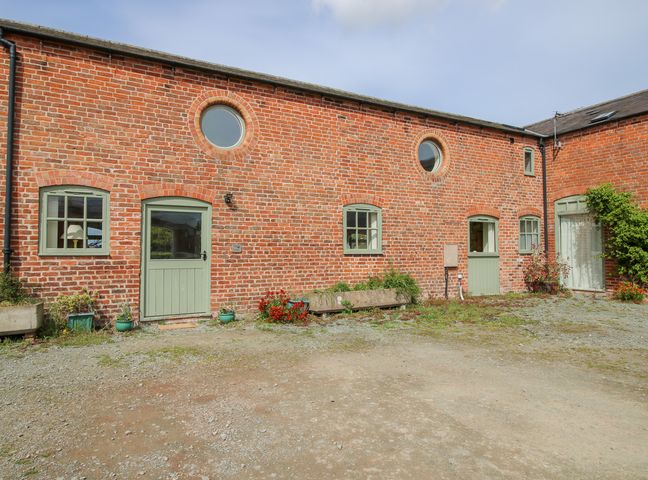 The exterior of a red brick building with green doors and windows and some plants at Spinney View in Cockshutt