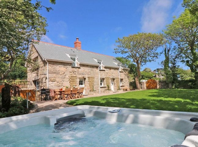 A stone house with outdoor dining furniture and a hot tub in the yard at The Old Forge in St Just
