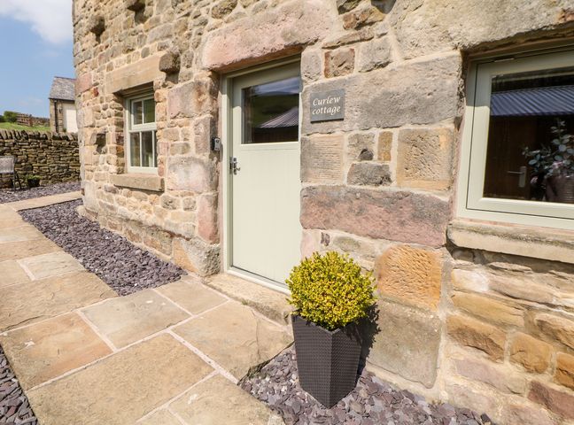 Stone exterior of a cottage with a door and two windows and a plant in a pot at Curlew in Longnor