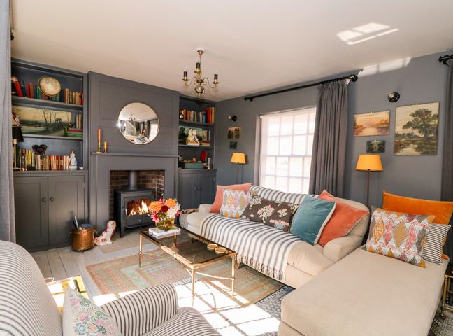 A living room with a fireplace a sofa with cushions a striped armchair and paintings on the wall at 12 Banks Street in Horncastle