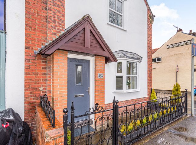 Front entrance of a brick and white house with a grey door and small garden behind a black wrought iron fence at Stablefold in York