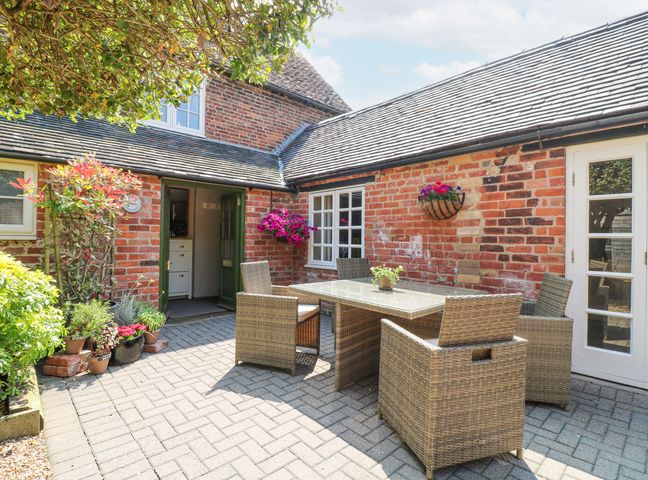 An outdoor patio area with a glass table and wicker chairs surrounded by brick walls and plants at The Creamery in Wychnor near Alrewas