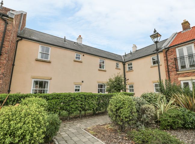 A building with multiple windows and a garden with shrubs and a paved pathway at Nett's Coastal Escape in Filey