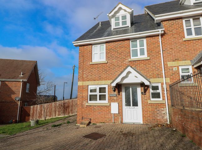 The front view of a red brick house with a white door and three white framed windows and a paved driveway at Hurst View in Yarmouth