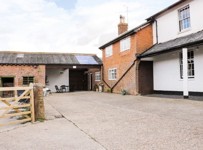 An outdoor courtyard with a brick building white building and wooden gate at Redwood Cottage in Lower Dean near Kimbolton