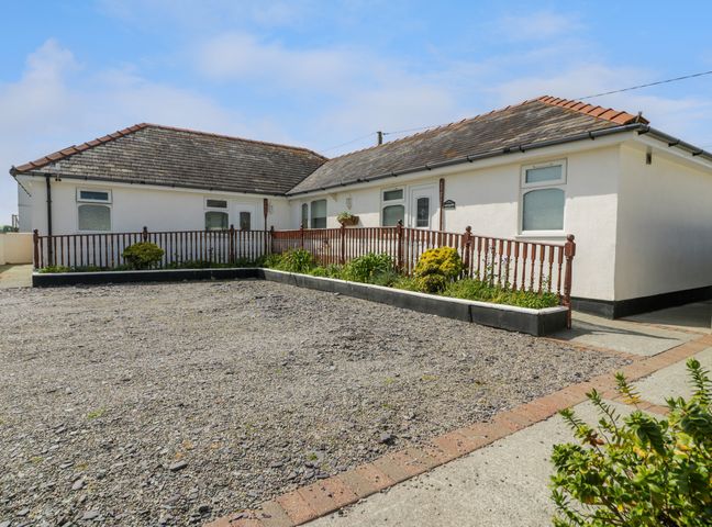 A single story building with a gravel driveway and a wooden railing with plants at Sea Breeze in Dinas Dinlle