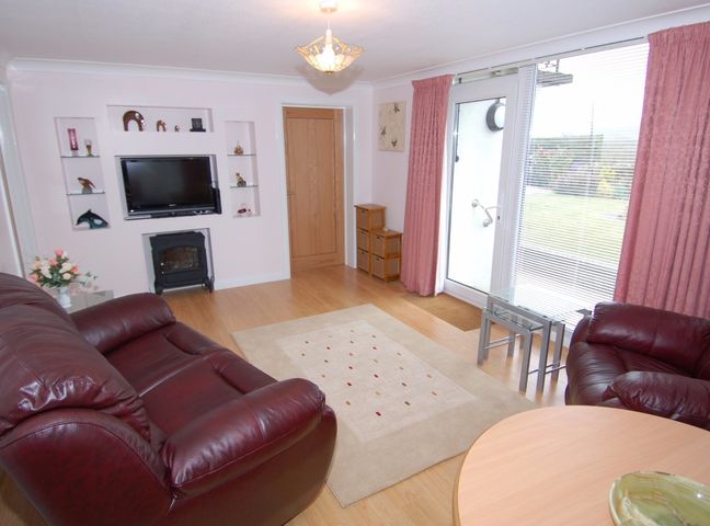 A living room with leather sofas a wall-mounted television and glass door with curtains at Garden View in Kingskerswell