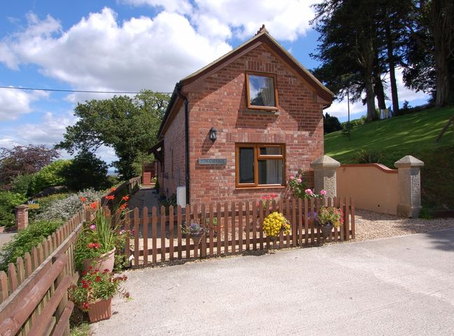 A brick cottage with wooden windows and a small garden behind a wooden fence at Ash Cottage in Longdown