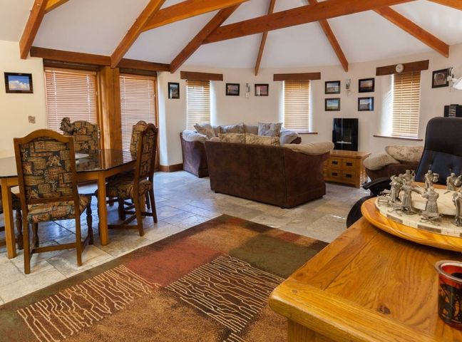 A living room with exposed wooden beams sofa set dining table with chairs and window blinds at Hideaway in Tintagel