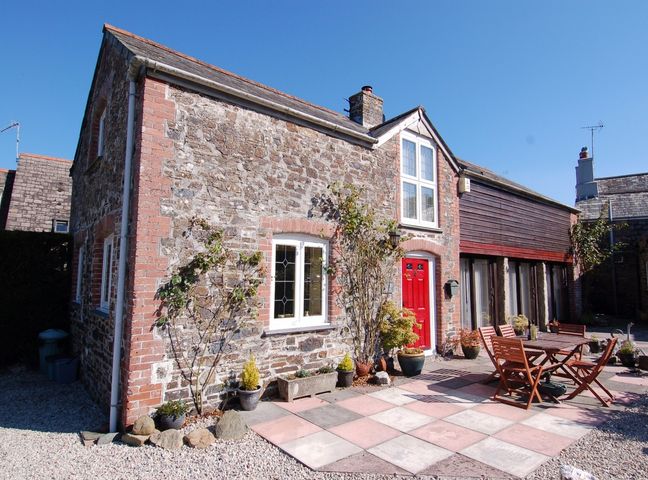 A stone and brick house with a red door and an outdoor patio with a wooden table and chairs at Jacobs Barn in Lifton