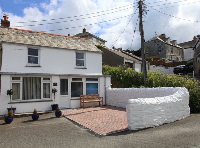 A white two-story house with plants in pots and a wooden bench outside at The Keep Pot in Port Isaac
