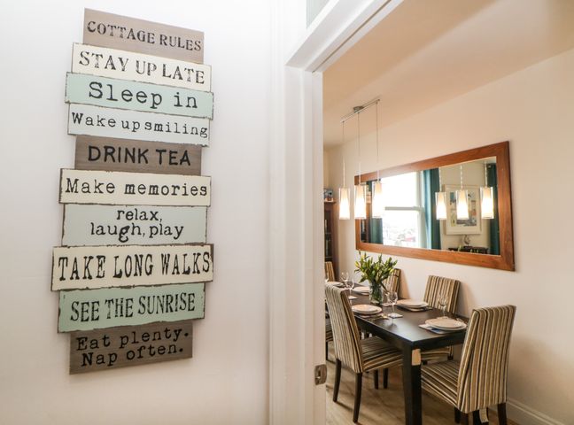 A dining room with a black table set for six and a large mirror on the wall with a sign displaying cottage rules on the adjacent wall at Quayside Lookout in Brixham