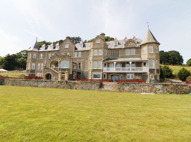 A large stone building with multiple windows and turrets surrounded by grassy land at Bryn Mel Apartment in Glyngarth