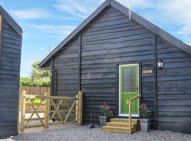 A wooden cabin with a green door and wooden steps at Woodpecker Lodge in Henley near Langport