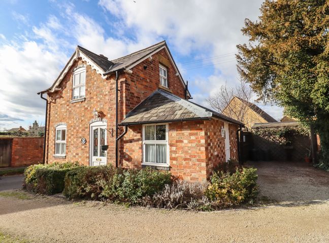 A red brick detached house with a gravel driveway and surrounding bushes at Elder Cottage in Mickleton near Chipping Campden