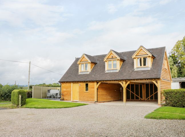 A wooden house with three dormer windows a gravel driveway and green lawn at Acorn Cottage in Little Hereford