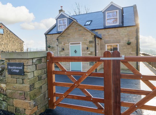 A front view of a stone cottage with a wooden gate and a sign reading Bramblewood Cottage in Middleton-In-Teesdale