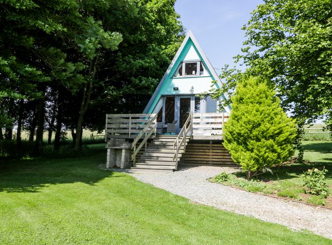 A small A-frame house with a wooden deck and stairs surrounded by trees and grass at Apple Tree Lodge in Gillingham
