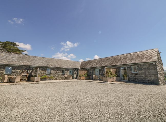 An outdoor view of a stone building with slate roof and patio seating at Cornel Glyd in Talybont near Barmouth