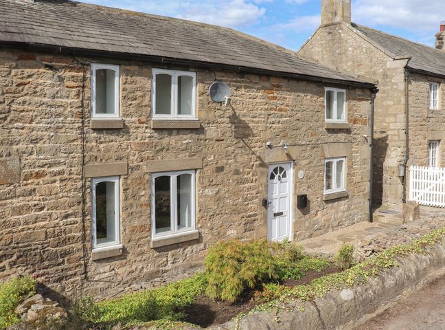 A stone cottage exterior with white windows and door surrounded by a small garden at 1 Dunkirk Cottages in Humshaugh near Hexham