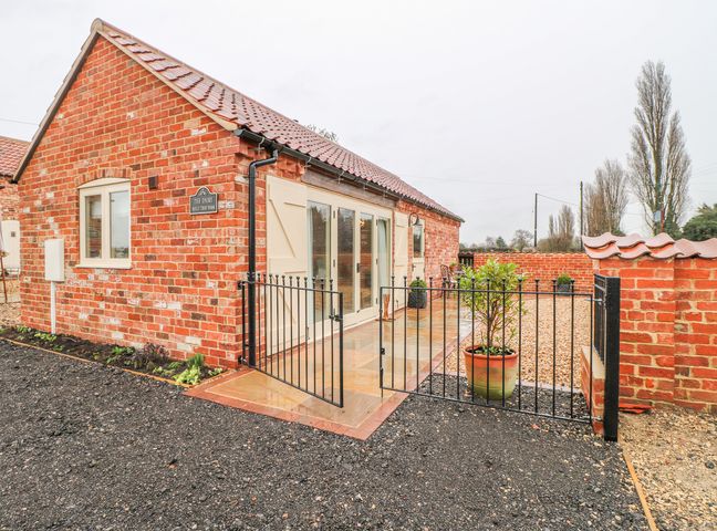 A brick building with a tiled roof a black metal gate and a patio with potted plants at The Dairy in North Scarle near Lincoln