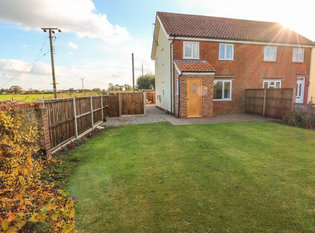A backyard with a lawn and wooden fences next to a semi detached house at 27 Whitegates in Ludham