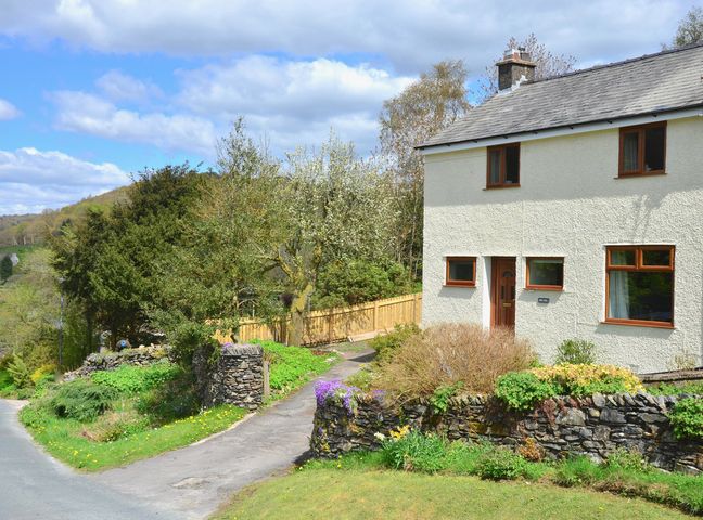 A house with stone walls and a garden next to a curved road at Ling Fell Cottage in Backbarrow