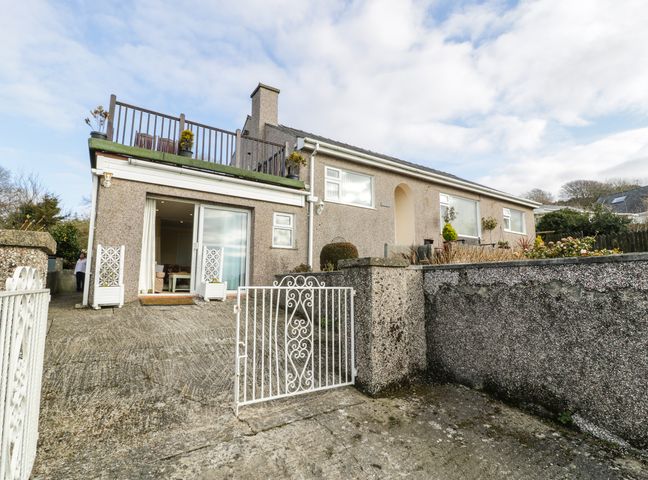 Exterior view of a one-story house with a concrete driveway a white gate and a terrace with potted plants at Maesawel Studio in Llanfair