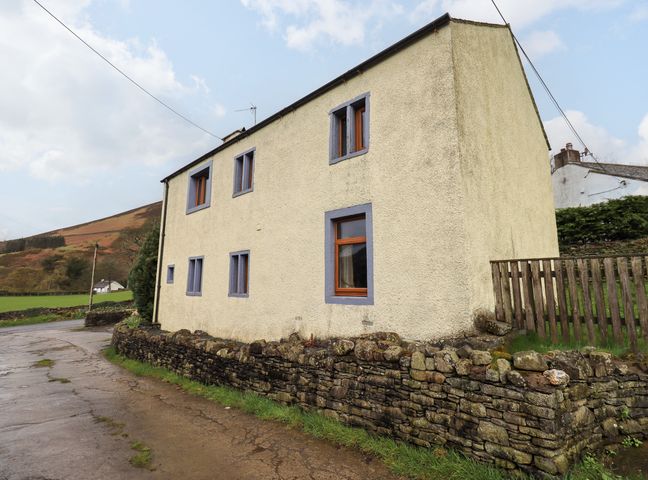 An exterior view of a two-story house with six windows and a stone wall in front at Scales Cottage in Lorton near Cockermouth