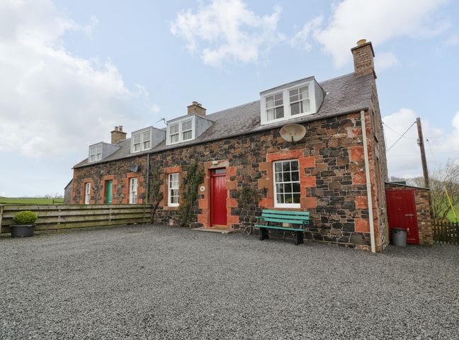 Exterior view of a stone cottage with red and green doors and windows with white frames at Craggs Cottage in Kelso Scottish Borders
