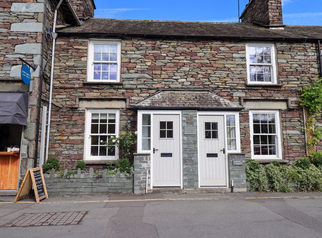 Two white doors and four windows on a stone cottage with plants in front at Beck Steps 1 in Grasmere