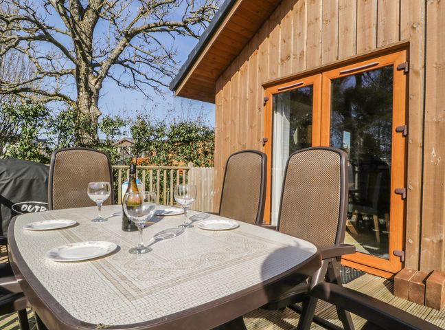 An outdoor table with plates and wine glasses set on a wooden deck outside a wooden building at Holmedell in Greystoke