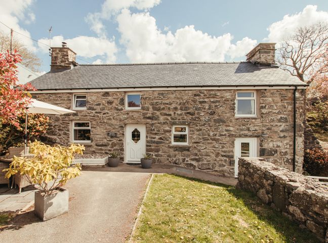 A stone cottage with white doors and windows and a small garden at Cefn Uchaf Cottage in Llanbedr